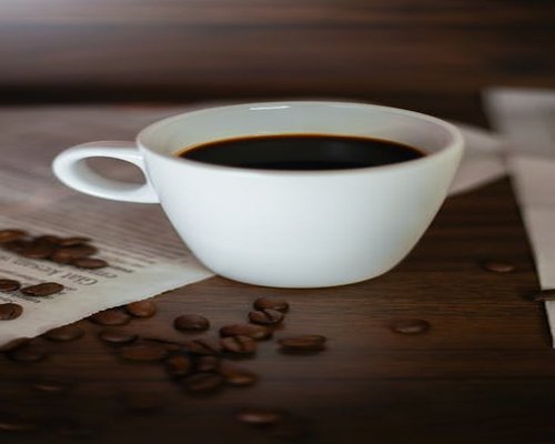 A simple white ceramic cup with freshly poured coffee on a table near organic roasted beans